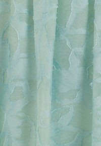 Kohde on läpinäkyvää kangasta vaalean mintunvihreänä, jossa on kohokuvioitu kukkakuosi. Pintakäsittely on sileä, ja kankaalla on hieno, virtaava laatu.