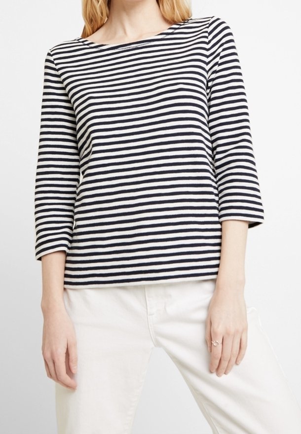 Camicia a maniche lunghe a righe con linee orizzontali blu navy e bianche, scollatura a barca e vestibilità comoda, abbinata a pantaloni chiari.