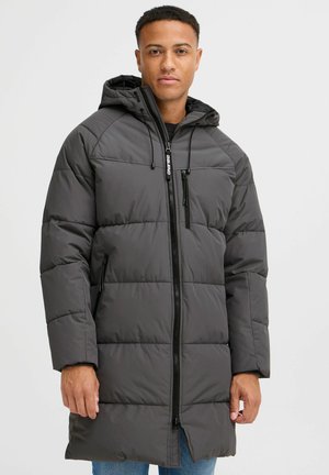Chaqueta acolchada gris con capucha, que cuenta con un cierre frontal, bolsillos laterales con cremallera y textura acolchada. Mangas largas con puños elásticos.