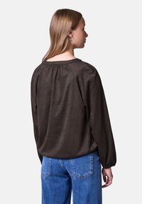 Mørkebrun bluse med en blød tekstur, rund halsudskæring og rynket detalje på ryggen, parret med blå denimjeans, vist fra ryggen.