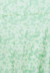 Tecido floral verde com uma textura suave, apresentando pequenas flores verdes claras e escuras sobre um fundo verde pálido, com uma qualidade ligeiramente translúcida.