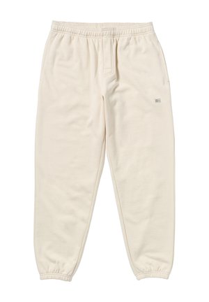 Pantalones de chándal color crema hechos de una tela suave, con una cinturilla elástica, tobillos ajustados y una pequeña etiqueta de logo en la parte frontal.