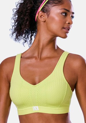 Athletic woman wearing a lime green sports bra and multicolored headband, looking right with curly hair tied back.