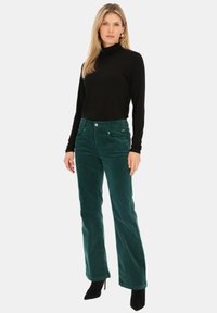 Zielone spodnie z kordurowej tkaniny o rozszerzonym fasonie, zestawione z czarną bluzką z długim rękawem. Outfit charakteryzuje się gładką teksturą i subtelnymi akcentami.