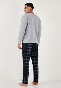 Camiseta de manga larga gris combinada con pantalones de pijama de cuadros azul marino con líneas de rejilla blancas. El diseño es de corte relajado con cuello redondo.