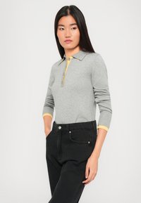 Polo gris à manches longues avec un col jaune et une patte de boutonnage à trois boutons, associé à un jean noir taille haute, doté de poches latérales.