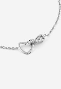 Collana d'argento con un simbolo dell'infinito a forma di cuore, adornata con cristalli trasparenti lungo un lato, attaccata a una catena a maglie.
