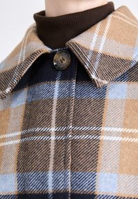 Plaid wool coat featuring tan, blue, and dark brown colors. Notable details include a broad collar, a black button, and soft texture.