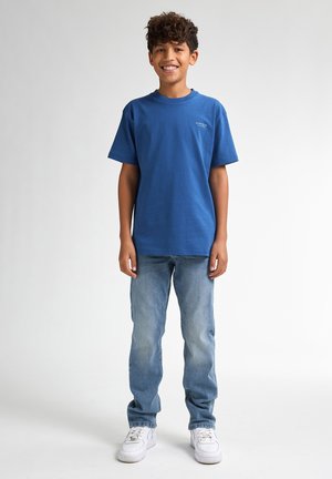 Blauwe katoenen T-shirt met korte mouwen, ronde halslijn en een klein logo; gecombineerd met licht verwerkte spijkerbroek en witte sneakers.