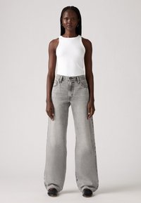 Lichtgrijze wijde jeans met een hoge taille, gemaakt van denim. Gecombineerd met een aansluitend wit tanktop, weergegeven tegen een neutrale achtergrond.