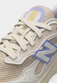 Μπεζ και κρεμ αθλητικό παπούτσι από δίχτυ με λευκά κορδόνια, μπλε περιμετρικό λογότυπο "N" και επενδεδυμένη γλώσσα με κίτρινη ετικέτα "Fresh Foam".