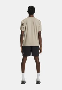 Svetlo béžové atletické tričko s krátkymi rukávmi, v kombinácii s čiernymi šortkami. Oblečenie sa vyznačuje hladkým materiálom a minimalistickým dizajnom.