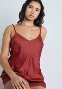 Camisole en satin rouge avec des bretelles réglables et un décolleté en V, accompagnée de shorts rouge avec une finition en dentelle. Texture lisse avec un éclat subtil.