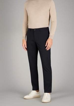 Marineblaue Hose mit taillierter Passform, aus leichtem Material gefertigt. Sie verfügt über einen Knopfverschluss und schräg geschnittene Fronttaschen, kombiniert mit weißen Sneakern.