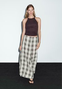 Top a halterneck marrone abbinato a una lunga gonna a quadri nei toni crema e grigio, con un design fluido e sandali neri con cinturini.