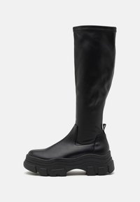 Bottes noires montantes en matériau synthétique lisse avec une semelle épaisse et des détails de couture le long du bord supérieur.