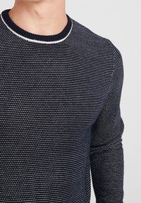 Maglione blu navy con un motivo di maglia testurizzato, caratterizzato da un collo a costine con rifinitura bianca e maniche lunghe.
