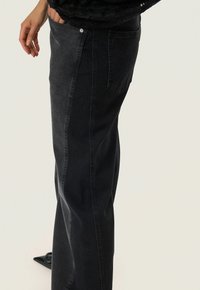 Dunkelblaue Jeans mit geradem Bein, ausgestattet mit einer Seitentasche und einem klassischen Knopfverschluss. Sanfte Textur mit minimalen Details.