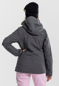 Grijze, gestructureerde winterjas met een capuchon, gecombineerd met lichtroze broek. Bevat een logo op de bovenrug, zwarte muts met een groene accent.