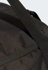 Bolsa de viaje de tela negra con superficie texturizada, equipada con una correa duradera y cierre de cremallera. Diseño sencillo y funcional sin adornos.