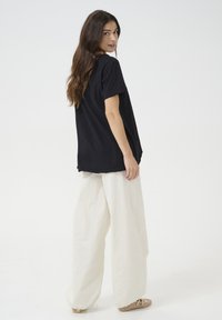 T-shirt noir en coton à manches courtes, associé à un pantalon en lin blanc ample. La tenue présente une coupe décontractée et une texture subtile.