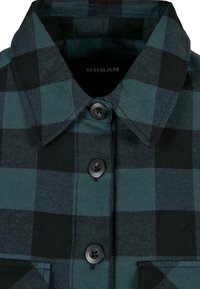 Gros plan sur une chemise à carreaux vert foncé et noire avec col et trois boutons noirs sur le devant.