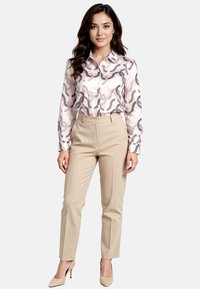 Light pink blouse with gray abstract pattern, paired with beige tailored trousers and nude high heels, standing against a neutral background.