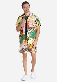 Multicolored short-sleeve shirt and shorts set featuring bold tropical patterns in yellow, pink, green, and blue. Cotton blend, relaxed fit.