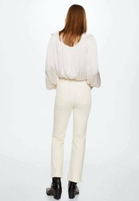 Blouse blanche plissée avec des manches bouffantes, associée à un pantalon ajusté taille haute couleur crème et des bottines à talons noires.