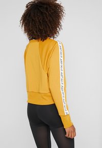 Żółta bluza z krótkim krojem, ribbotał hem i długimi rękawami, z białą taśmą "JUST DO IT" wzdłuż boków. Czarne legginsy.