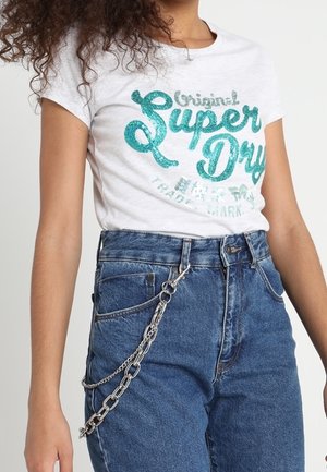 White t-shirt with teal "Super Dry" logo worn with high-waisted blue jeans and silver chain accessory hanging from belt loop.