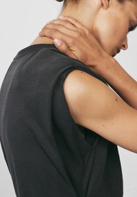 Kvinna i mörk ärmlös topp som rör vid nacken, med huvudet lutat ner, visar överarmen och profil.