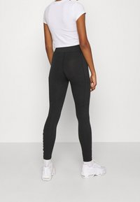 Svarta leggings med hög midja, tillverkade av stretchigt material, med sidofickor och vita logodetaljer längs benet.