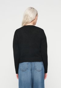 Juoda megzta megztinys su apvalia iškirpte, su raižytais detalėmis ir laisvu siluetu. Sukomponuota su aukštai juosmeniu, šviesiai mėlynos spalvos džinsais.