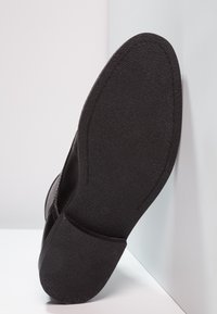 Sole di scarpa nera con una finitura texturizzata, caratterizzata da un contorno liscio e una leggera curvatura, su uno sfondo chiaro.