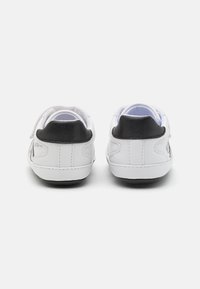 Białe sneakersy z czarnym akcentem na pięcie, gładka skórzana tekstura, wzmocnione przeszycia i rzepy zapewniające pewne dopasowanie.