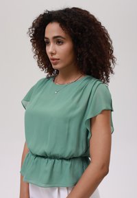 Grønn chiffonbluse med korte viftende ermer, innsnevret liv og myk, flytende tekstur. Enkel design med et lett utseende.