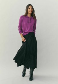 Purple knitted pullover with a collar and button detail, paired with a black pleated skirt, accessorized with black ankle boots.