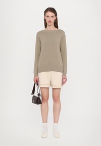 Beige strikket genser med vid hals, kremfargede shorts med strukturert finish, hvite sokker og en liten blank mørk håndveske.