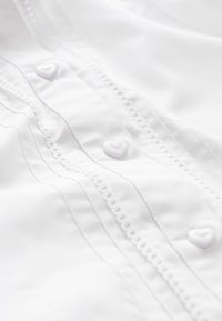 Tissu blanc avec des surpiqûres décoratives et de petits boutons en forme de cœur le long de la couture.