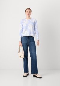 Lyseblå genser med blomsterdesign, vide blå jeans, kremfarget håndveske og loafers med svarte såler. Glatte teksturer og uformelt design.
