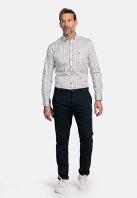 Witte hemd met knoopsluiting en een klein multicolor stippenpatroon, in combinatie met donkerblauwe broek en witte sneakers. Casual pasvorm en modern ontwerp.