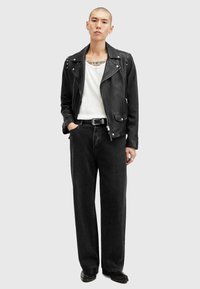 Jachetă de motociclist din piele neagră cu știfturi argintii, tricou alb, blugi negri cu croială lejeră și cizme negre. Accesorii minimaliste, design elegant.