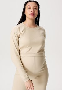 Beige Langarmshirt aus weichem, dehnbarem Material, mit rundem Halsauschnitt und figurnaher Passform. Glatte Textur ohne Muster oder Verzierungen.