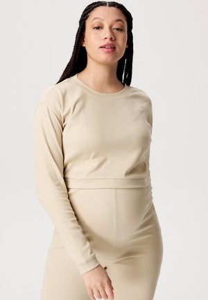 Beige Langarmshirt aus weichem, dehnbarem Material, mit rundem Halsauschnitt und figurnaher Passform. Glatte Textur ohne Muster oder Verzierungen.