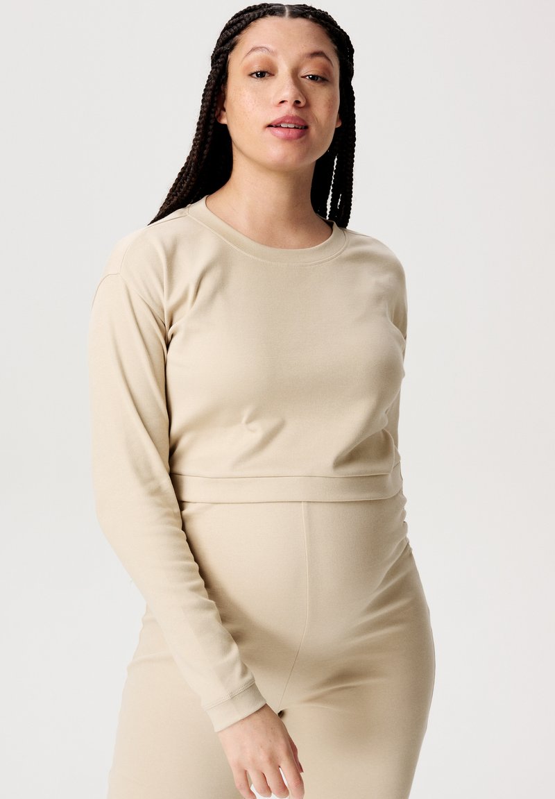 Beige Langarmshirt aus weichem, dehnbarem Material, mit rundem Halsauschnitt und figurnaher Passform. Glatte Textur ohne Muster oder Verzierungen.