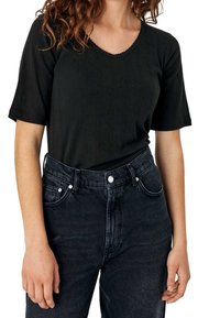 Mustapaita lyhyillä hihoilla ja V-pääntiellä, jossa on hienovarainen raidoitus. Yhdistetty korkeavyötäröisiin tummiin farkkuihin, joista löytyy hopeiset napit.