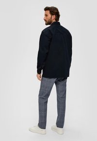 Camicia navy a maniche lunghe con colletto, abbinata a pantaloni a quadri grigi chiari e sneakers bianche, vista da dietro.