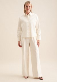 Weißes, button-up Hemd mit Kragen und langen Ärmeln, kombiniert mit lockeren, passenden Hosen. Glatte Stoffstruktur mit minimalen Akzenten.
