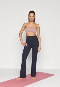 Ljusrosa sport-bh och mörkblå utsvängda yogabyxor, gjorda av elastiskt tyg, visade i stående position på en rosa yogamatta.